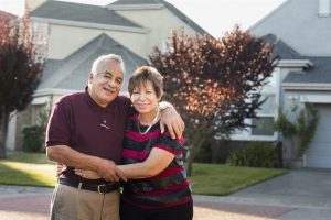 old couple looks happy in front of their home